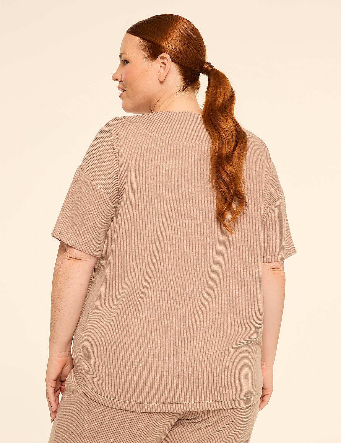 A woman with auburn hair pulled into a ponytail stands facing away from the camera in a beige ribbed t-shirt and matching pants against a plain beige background. Product Image 2