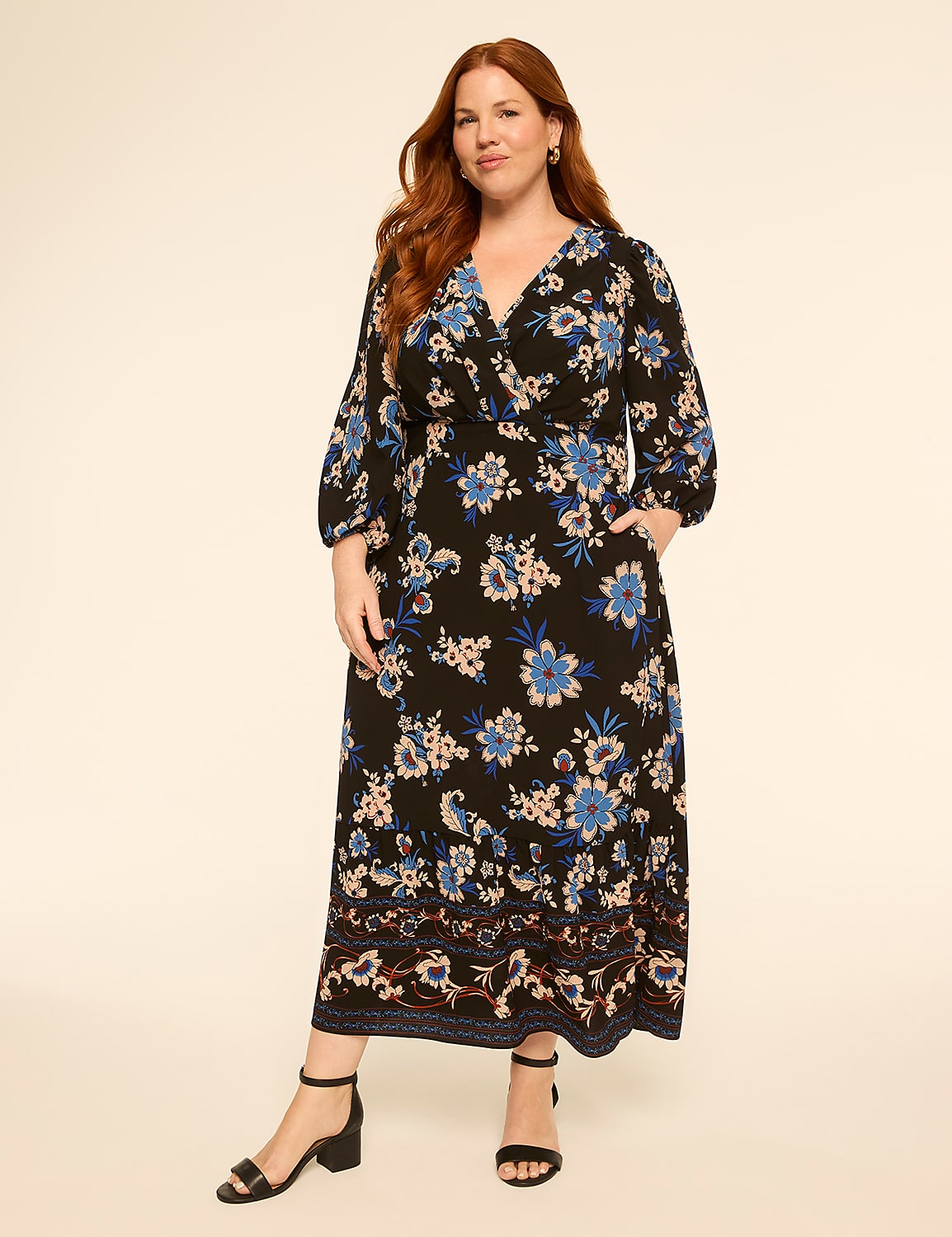 A woman with red hair stands in a black floral maxi dress with blue and pink flowers, against a plain, light-colored background. Product Image 1
