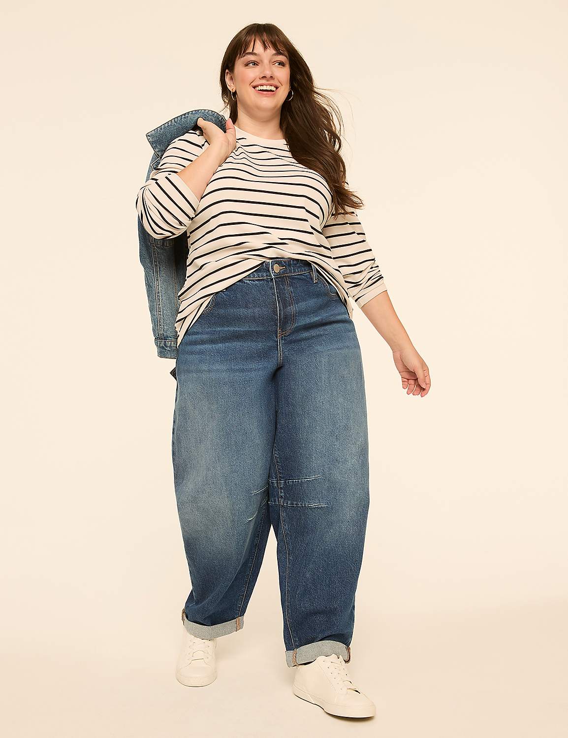 A smiling woman in a striped shirt and baggy jeans stands against a plain, light-colored background with a denim jacket slung over her shoulder. Product Image 3