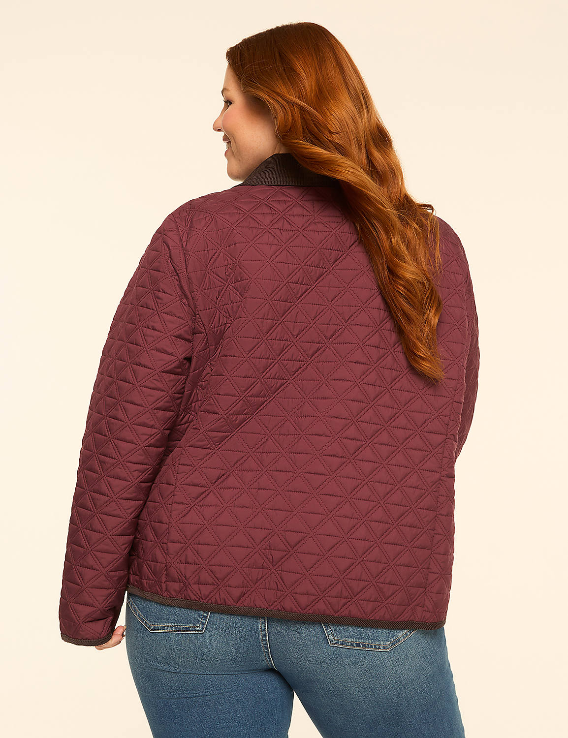 A woman with auburn hair wearing a quilted burgundy jacket and blue jeans stands against a plain, light-colored background. Product Image 2