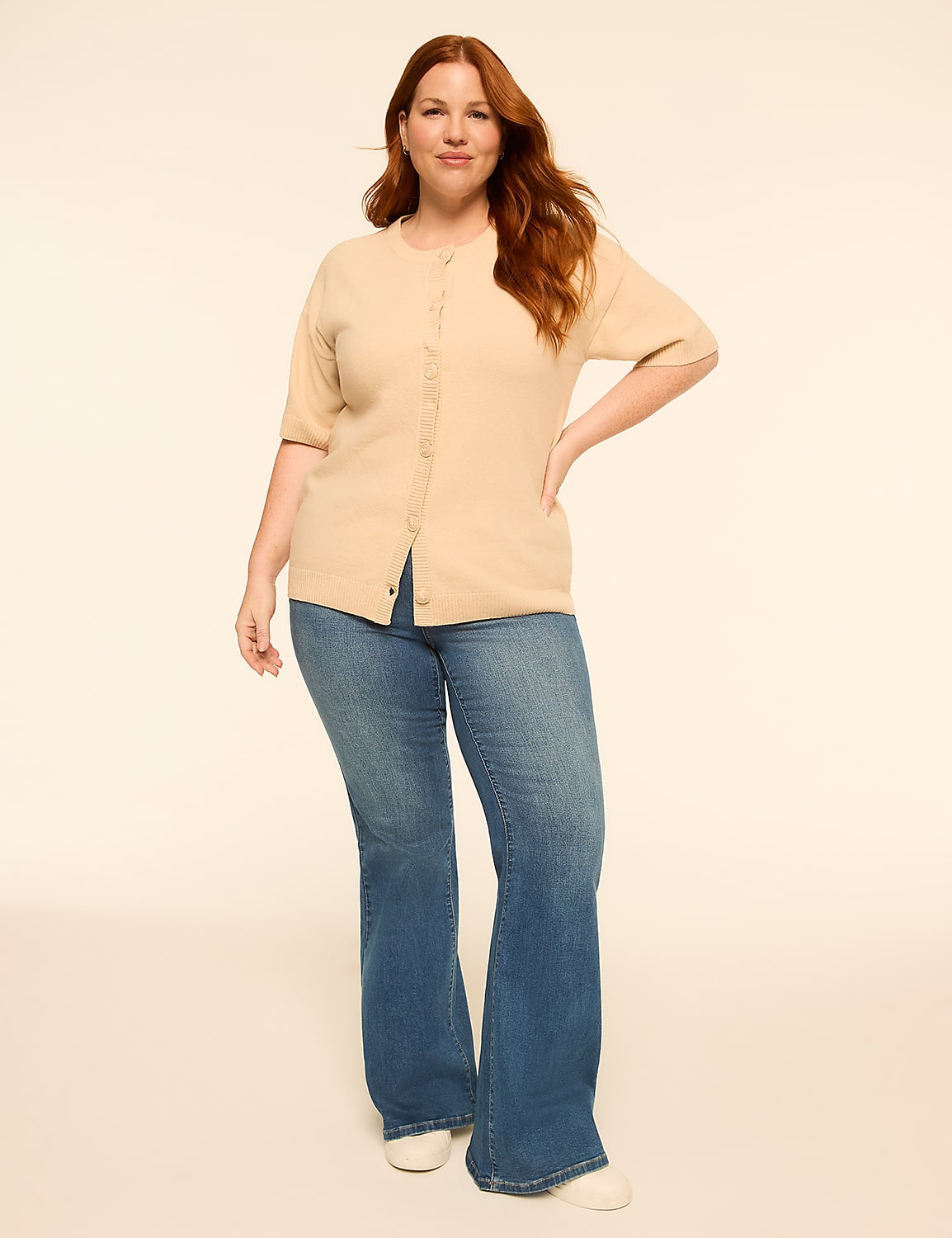 A woman with red hair stands in the foreground wearing a beige cardigan and blue jeans against a plain, light-colored background. Product Image 4