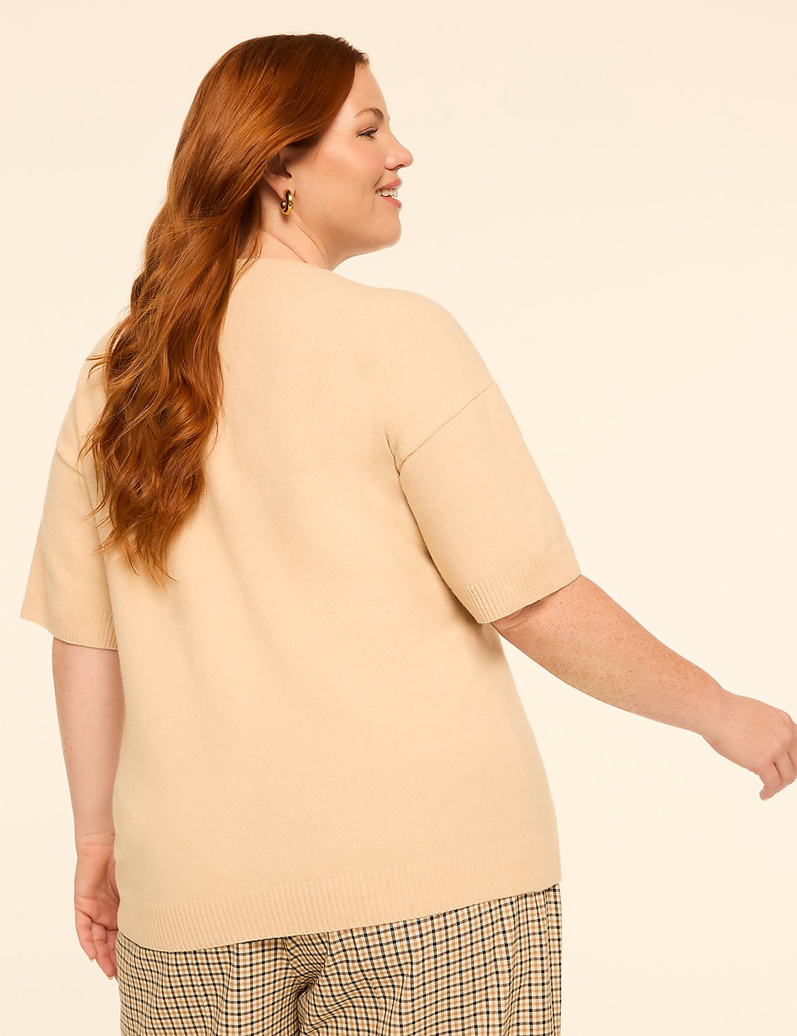 A woman with long red hair wearing a beige sweater and plaid pants turns away from the camera against a plain, light background. Product Image 2