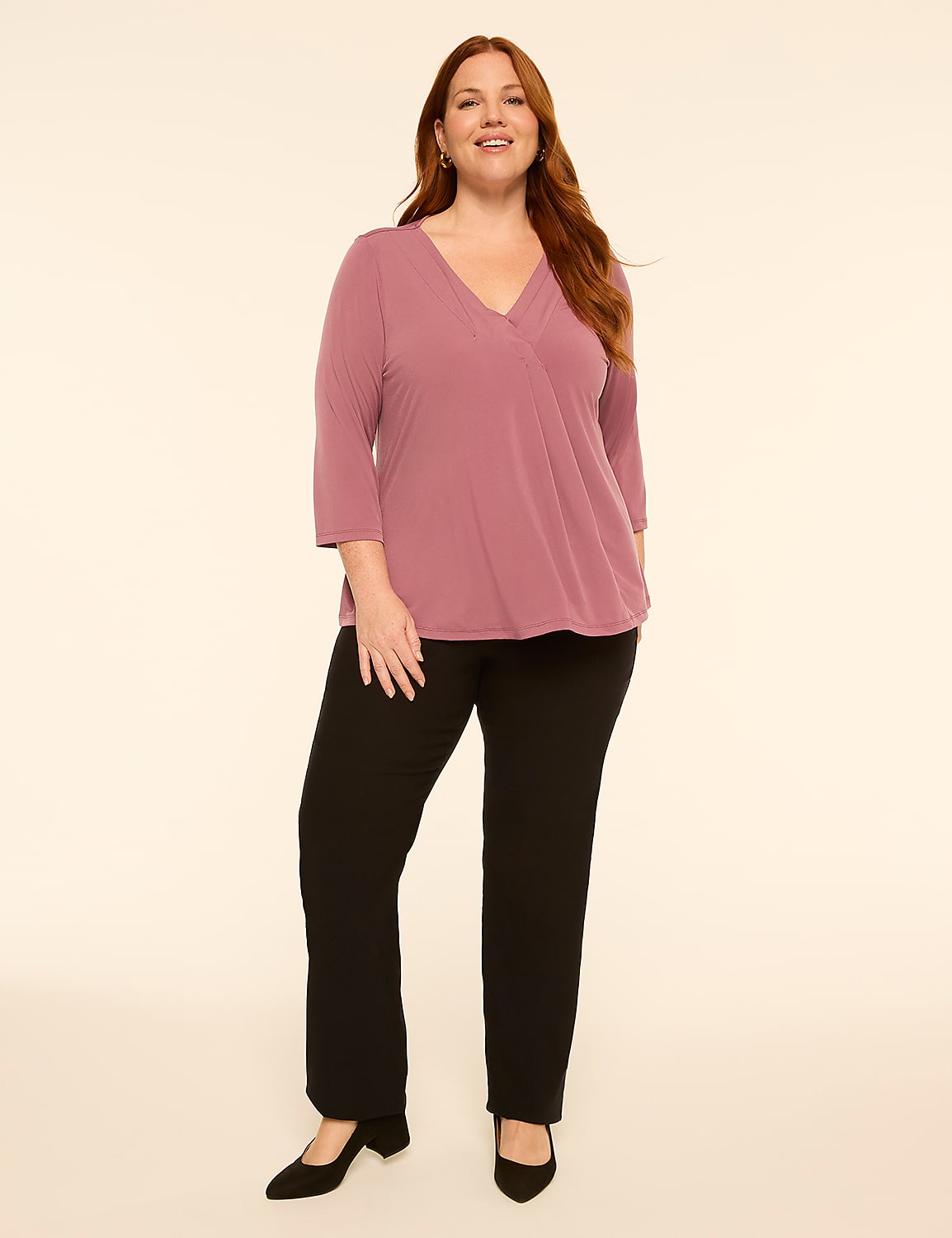 A smiling woman in a mauve wrap top and black pants stands against a plain, light-colored background. Product Image 3