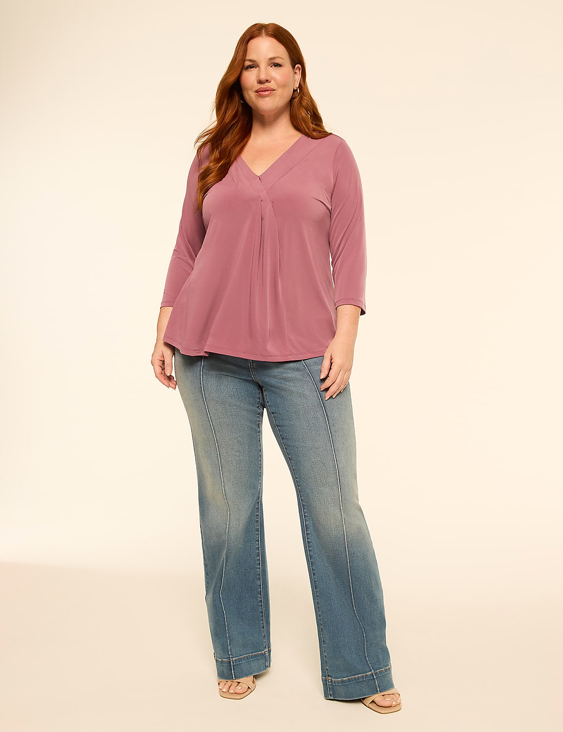 A woman with red hair stands in the foreground wearing a mauve v-neck top and flared jeans against a plain, light-colored background. Product Image 4
