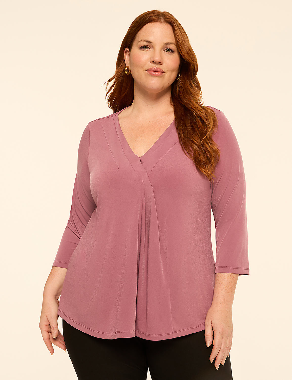 A woman with auburn hair and a mauve v-neck top stands against a plain cream background. Product Image 1