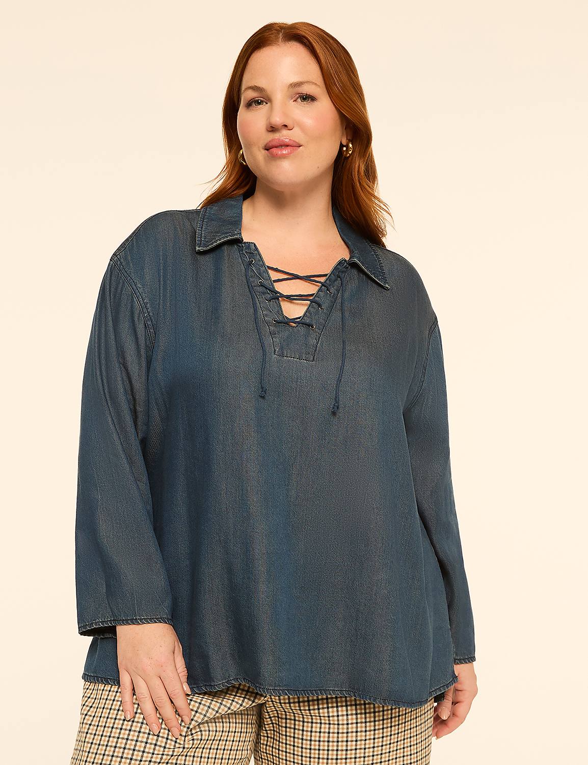 A woman with auburn hair and fair skin, wearing a blue denim lace-up shirt and plaid pants, stands against a plain beige background. Product Image 1