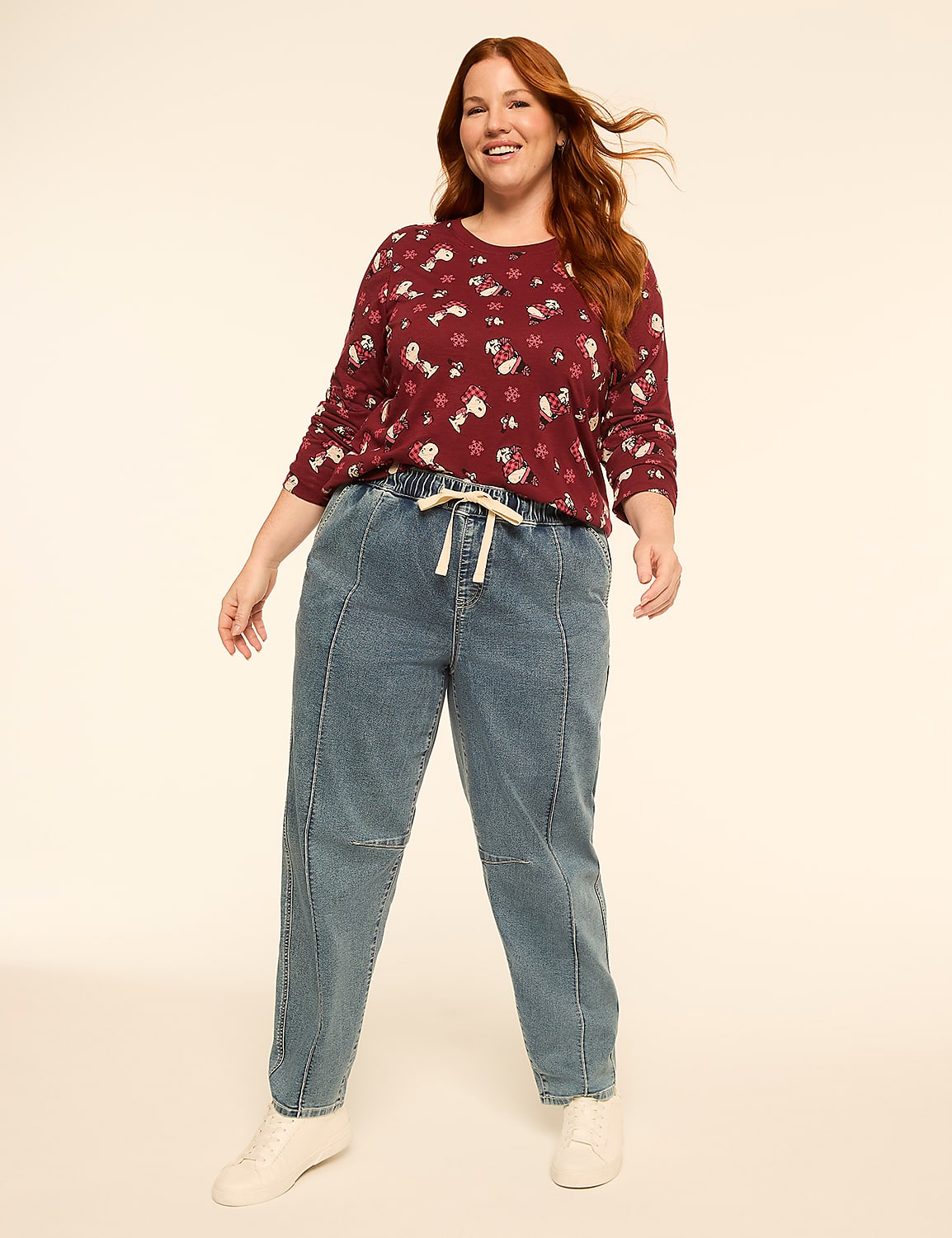 A smiling woman with red hair stands in the foreground wearing a maroon patterned top and blue jeans, against a plain, light-colored background. Product Image 3