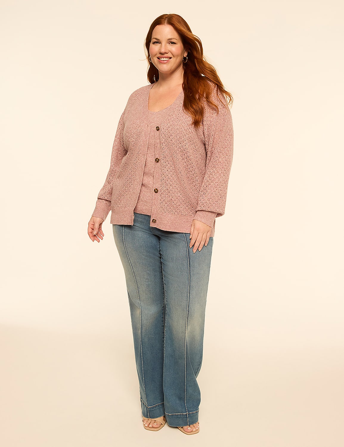 A smiling woman with red hair stands in the foreground wearing a pink cardigan and jeans against a plain, light-colored background. Product Image 3