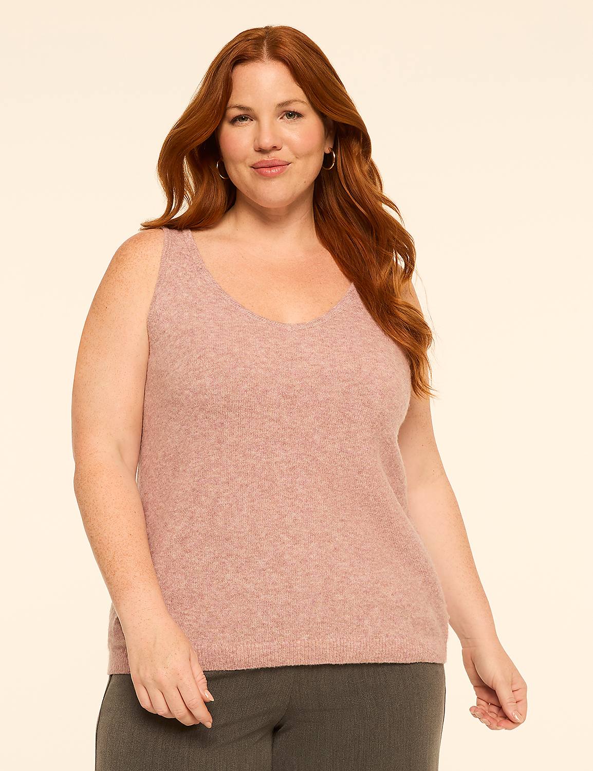 A smiling, red-haired woman in a pink v-neck sweater and grey pants stands against a plain, light-colored background. Product Image 1
