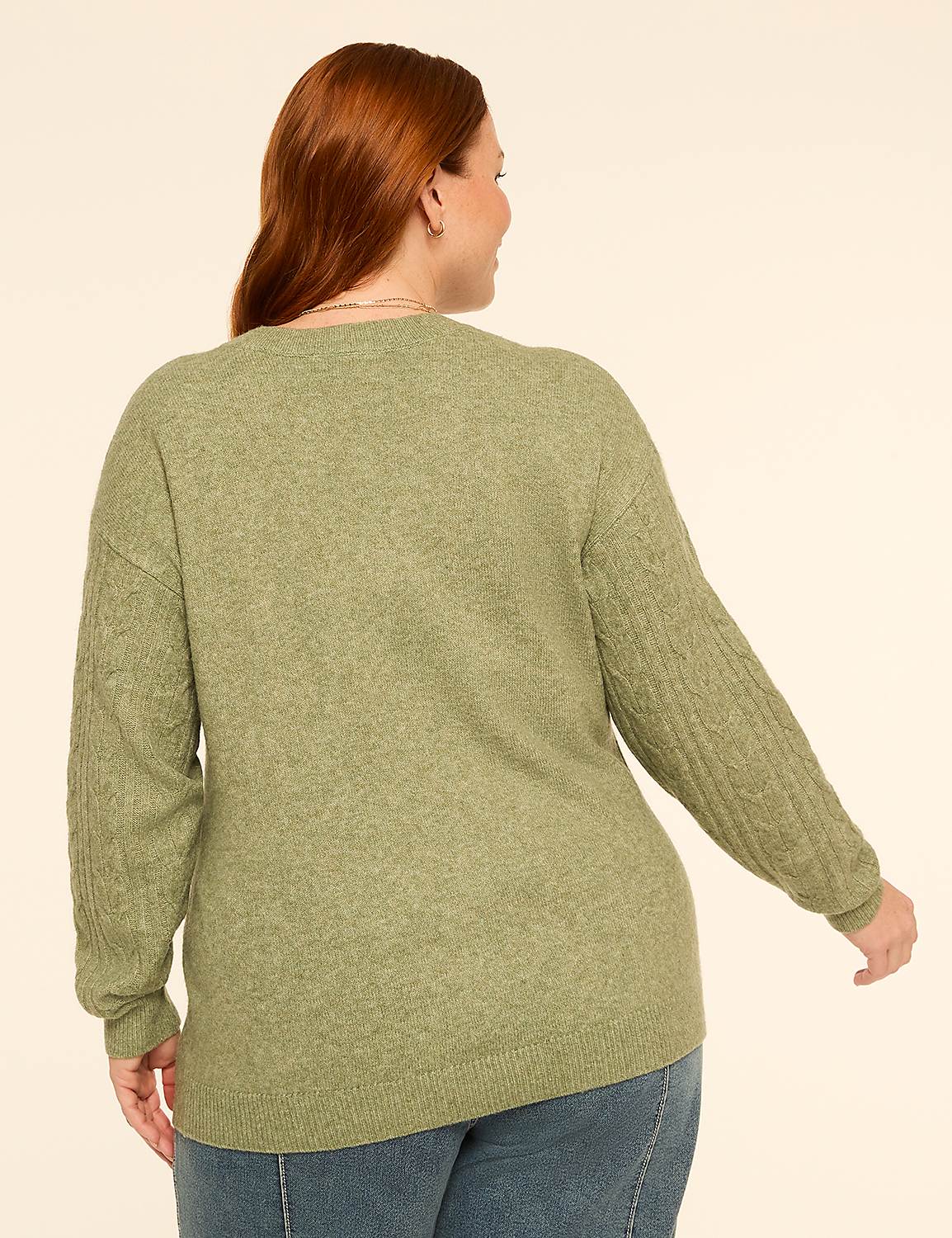 A woman with red hair wearing a green cable-knit sweater and blue jeans stands against a plain, light-colored background. Product Image 2