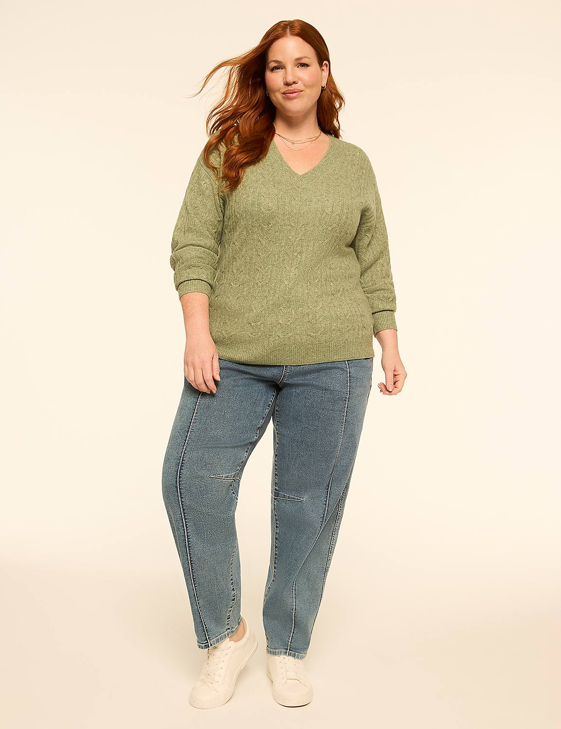 A woman with red hair stands in the foreground wearing a green sweater and blue jeans against a plain, light-colored background. Product Image 3