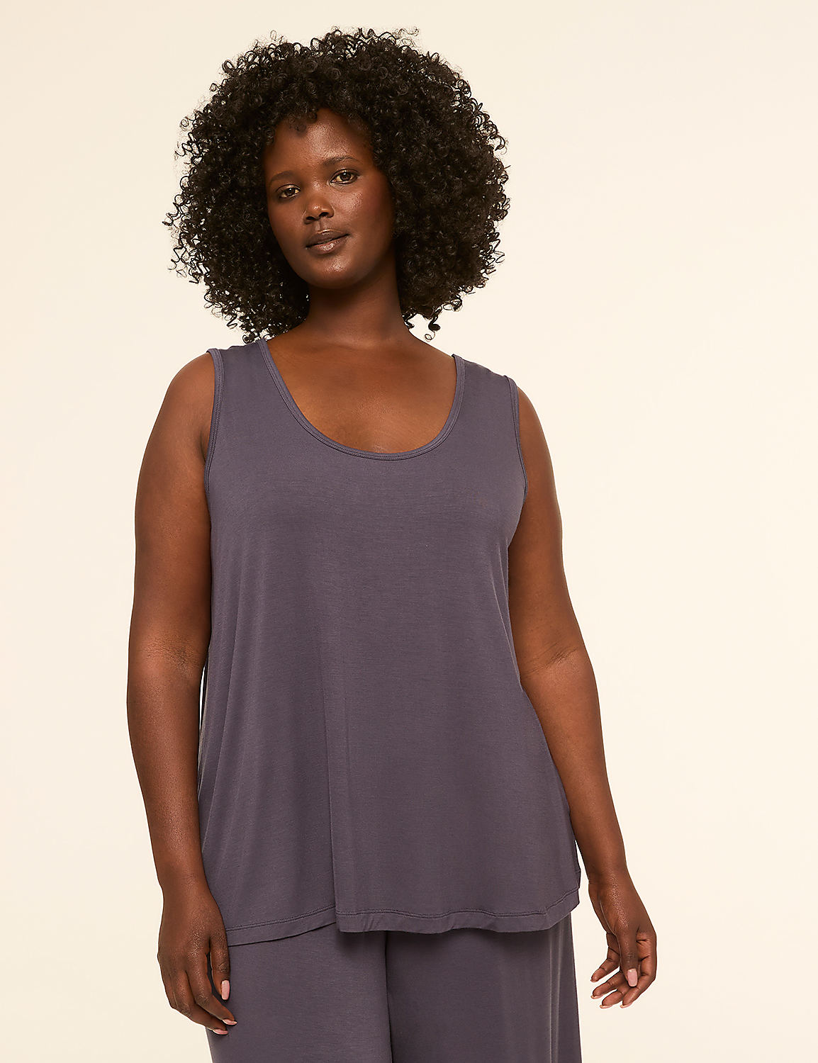 A woman with dark, curly hair and a gray tank top stands against a plain, light-colored background. Product Image 3