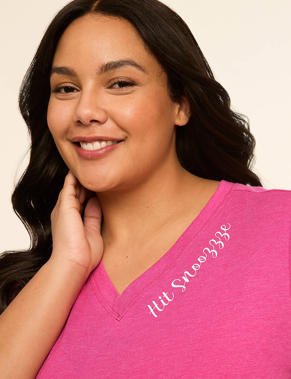 A smiling woman in a pink v-neck shirt with "Hit Snooozze" embroidered on it is shown against a plain, light-colored background. Product Image 4