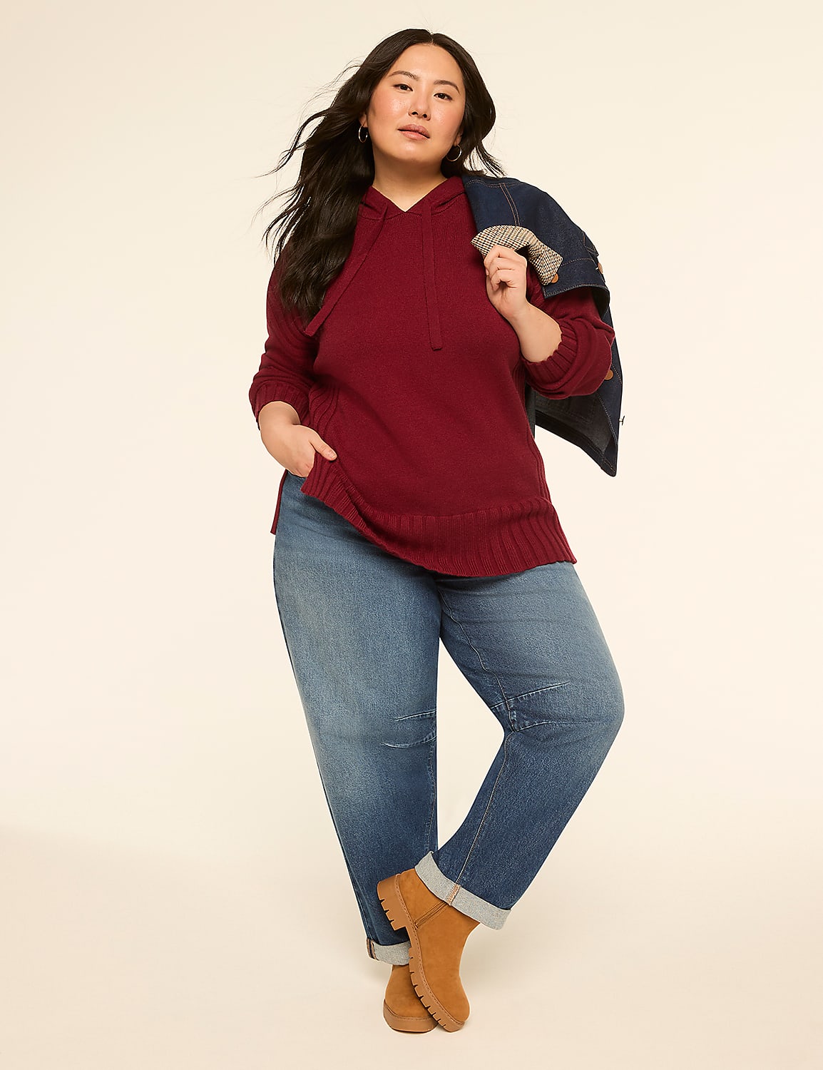 A woman in a maroon hoodie and jeans stands against a plain, light-colored background, with a denim jacket draped over her shoulder. Product Image 3