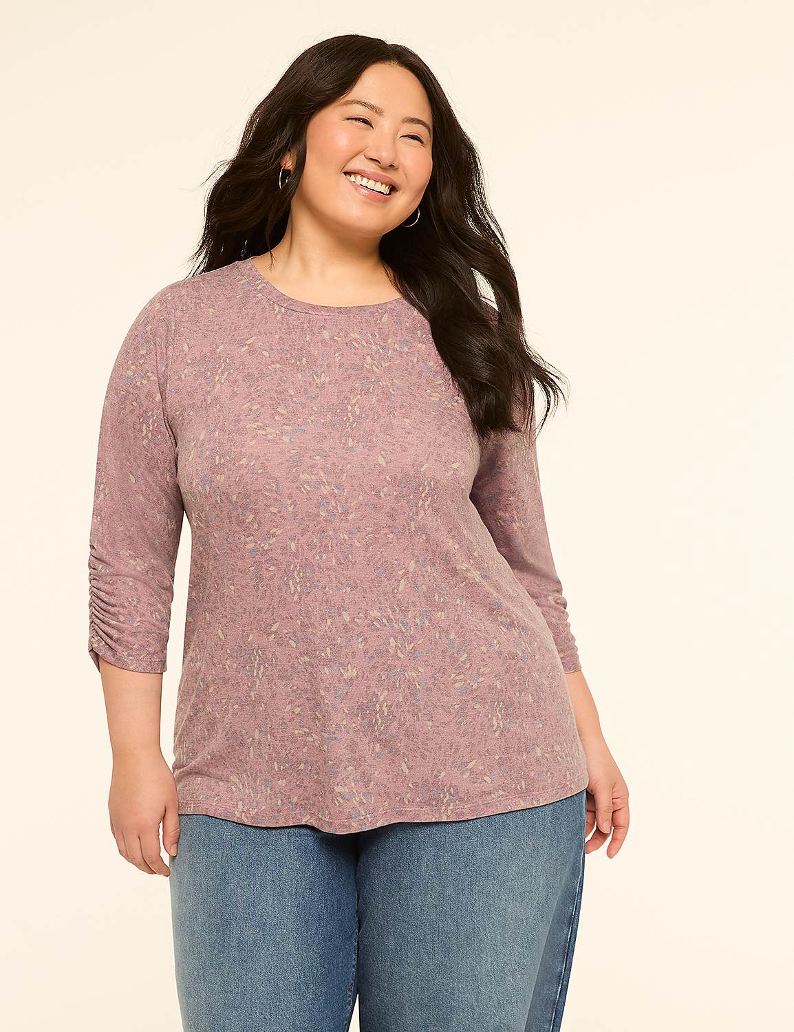 A smiling woman in a patterned pink shirt and blue jeans stands against a plain cream background. Product Image 1