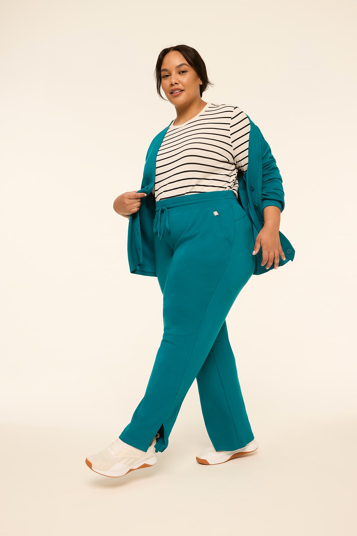 A woman in a teal cardigan, striped t-shirt, and matching teal pants with white sneakers stands against a plain, light-colored background. Product Image 5