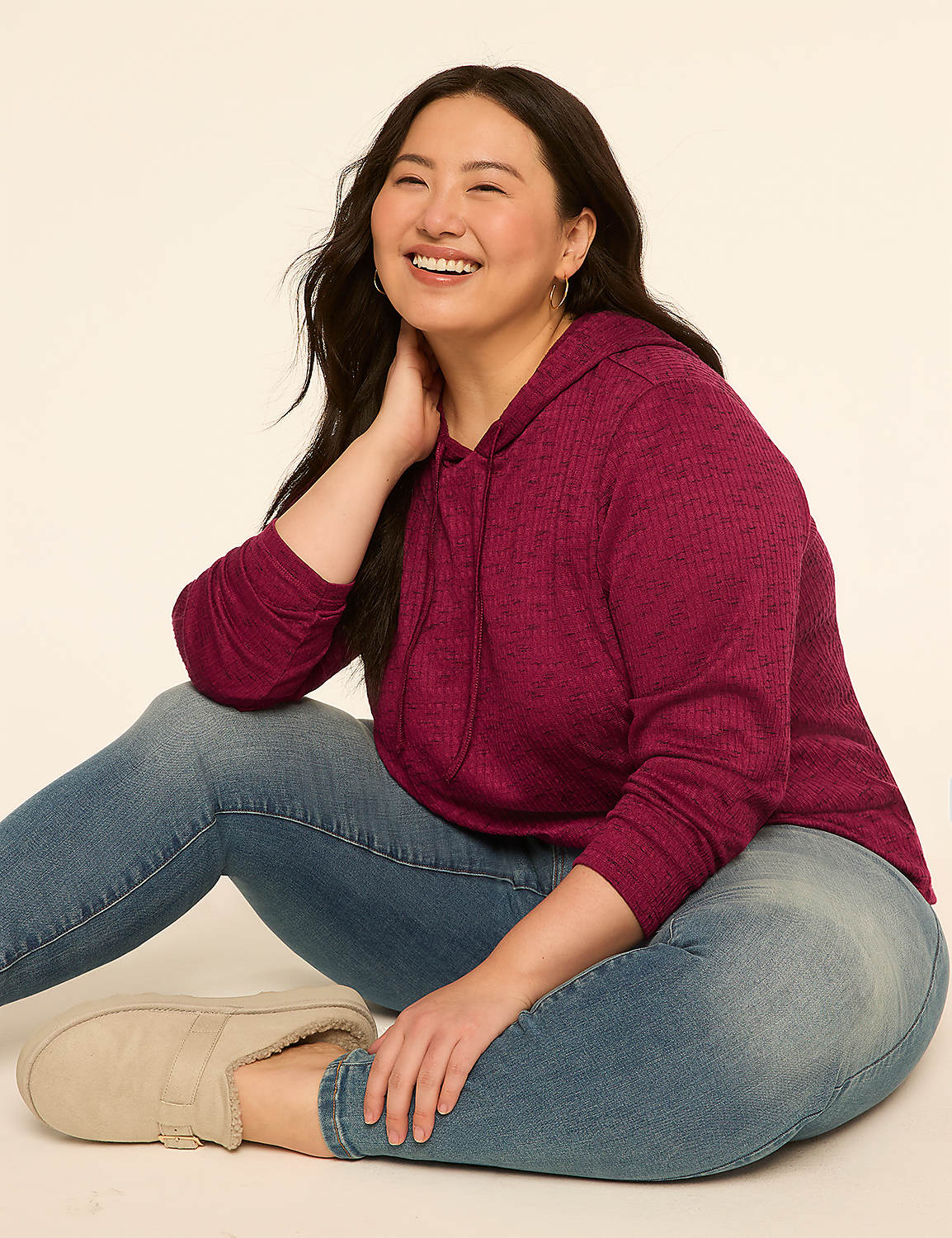 A smiling woman in a burgundy hoodie and jeans sits on a cream-colored floor against a plain cream background. Product Image 3