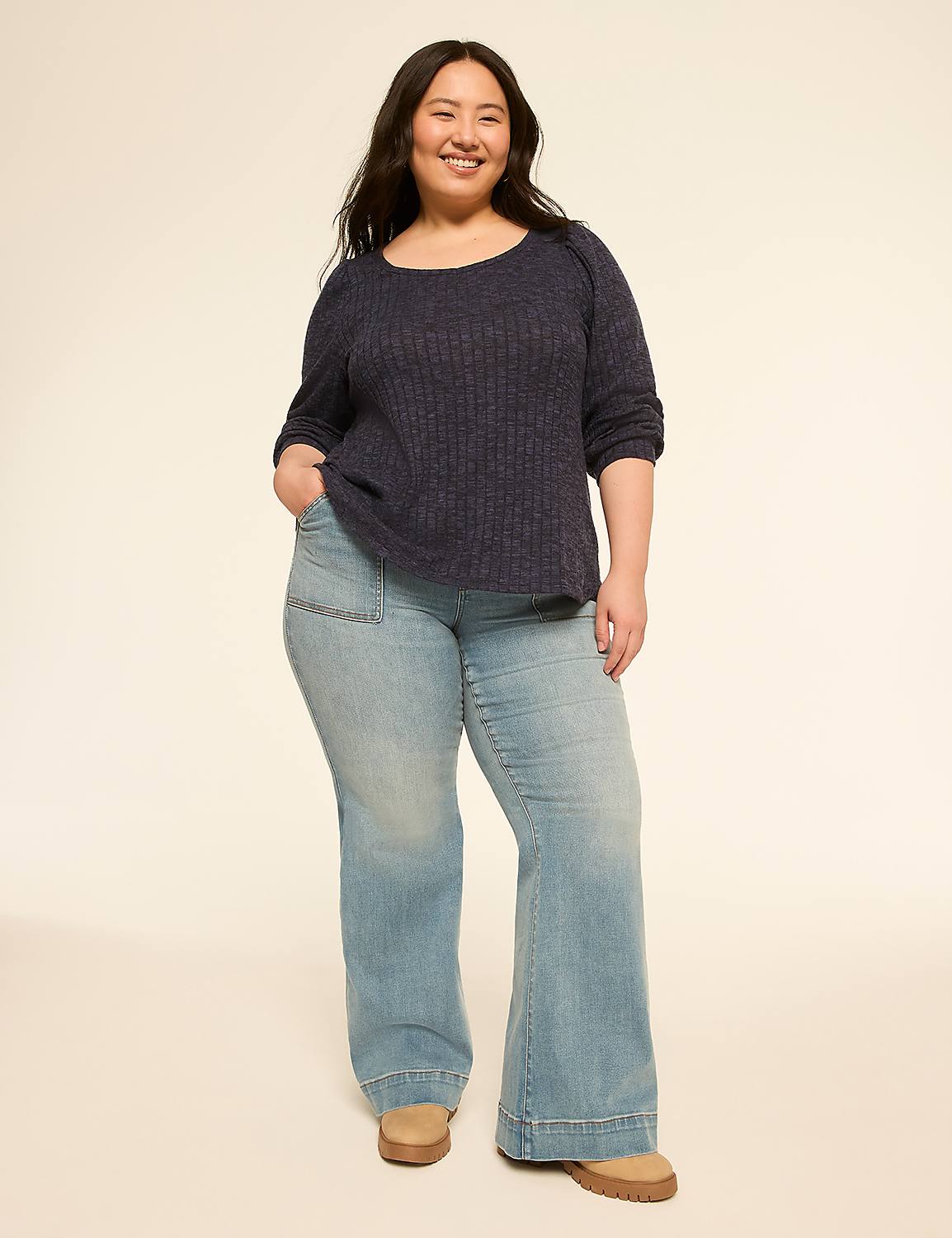 A smiling woman in a navy blue top and light wash flared jeans stands against a plain, light-colored background. Product Image 3