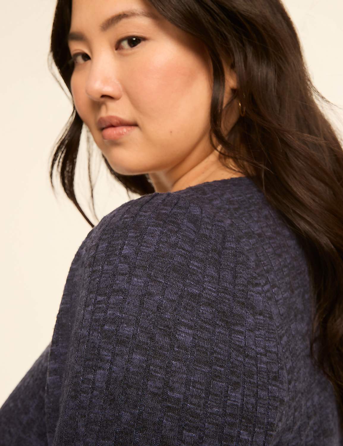 A woman with dark hair and a blue textured sweater is shown against a plain, light-colored background. Product Image 4