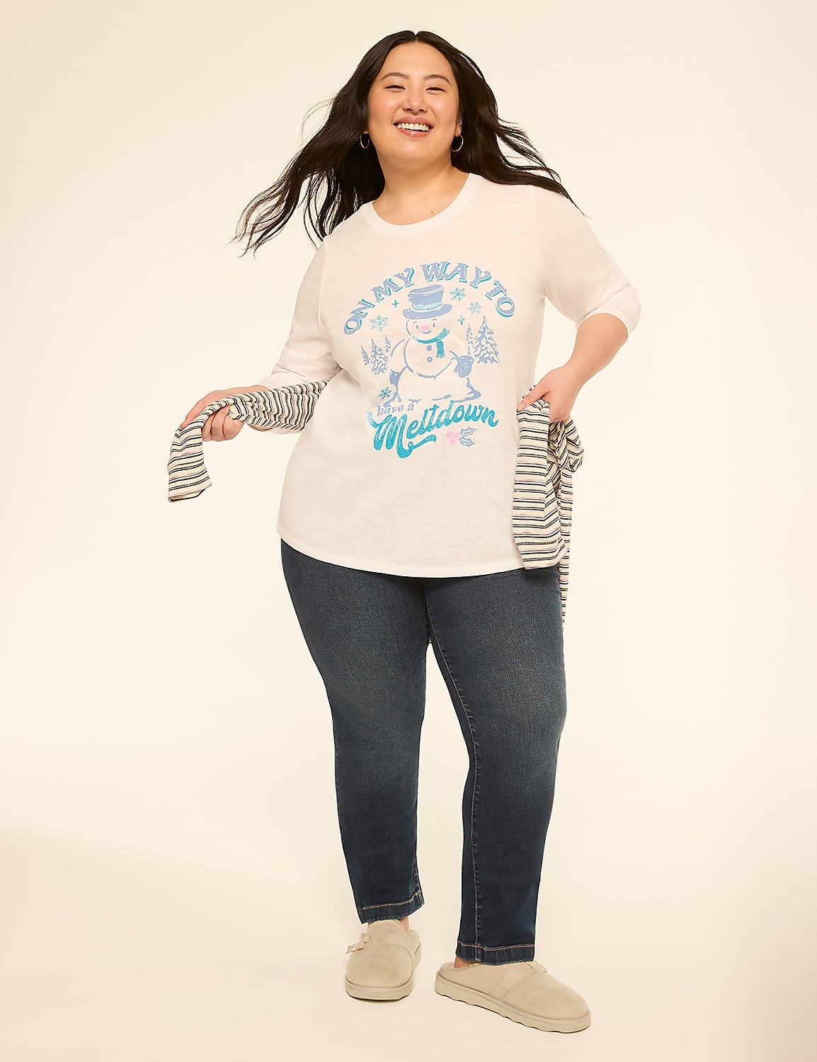 A smiling woman in a white graphic t-shirt and dark jeans stands against a plain, light-colored background, holding a striped scarf. Product Image 3