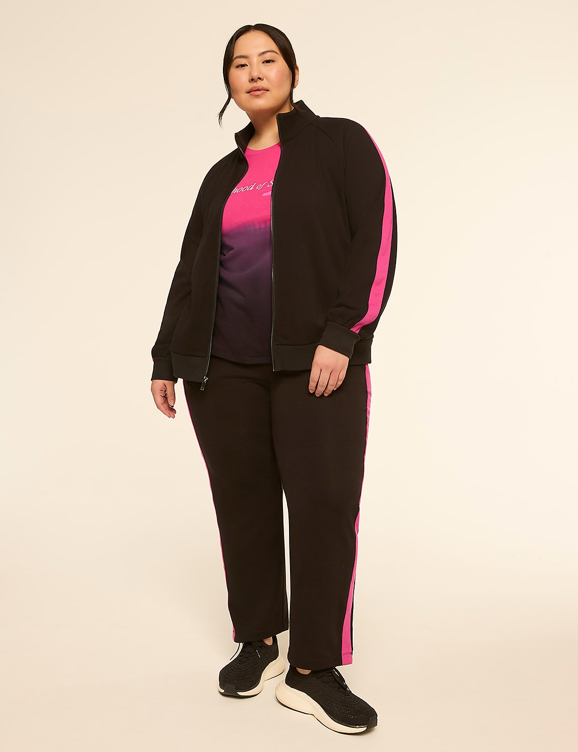 A woman in a black tracksuit with pink stripes stands against a plain, light-colored background. Product Image 3
