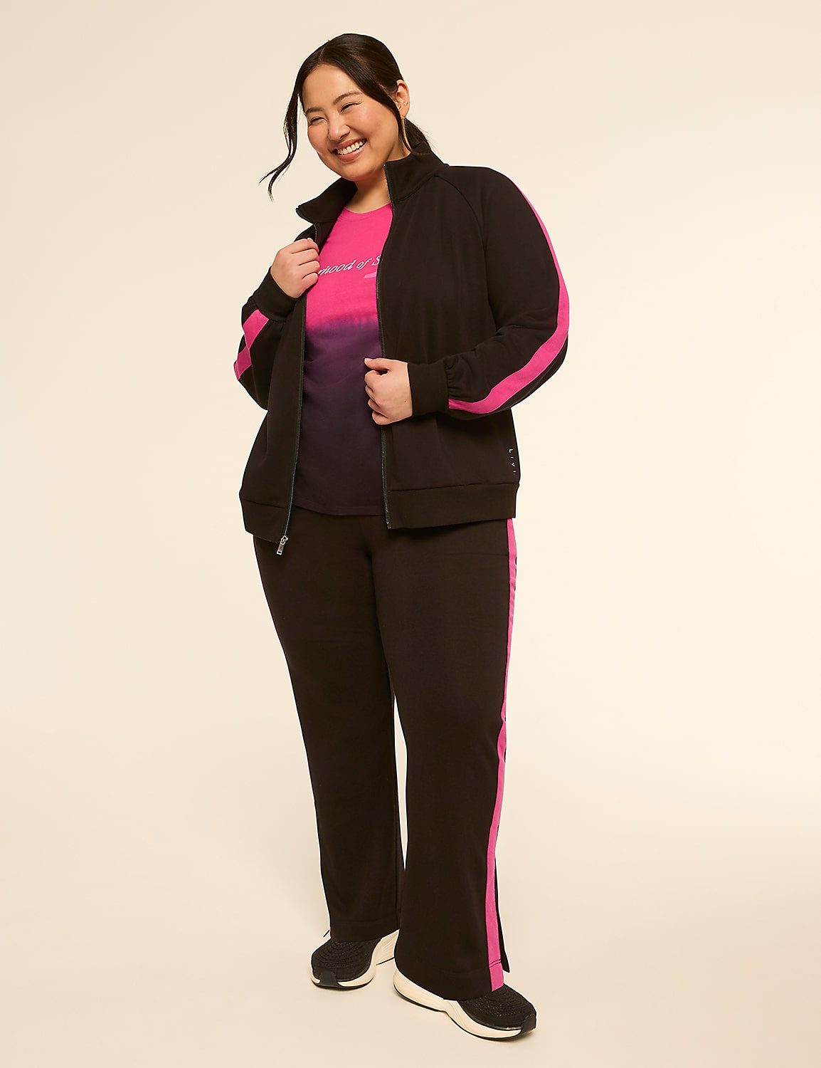 A smiling woman in a black tracksuit with pink accents stands against a plain, light-colored background. Product Image 3