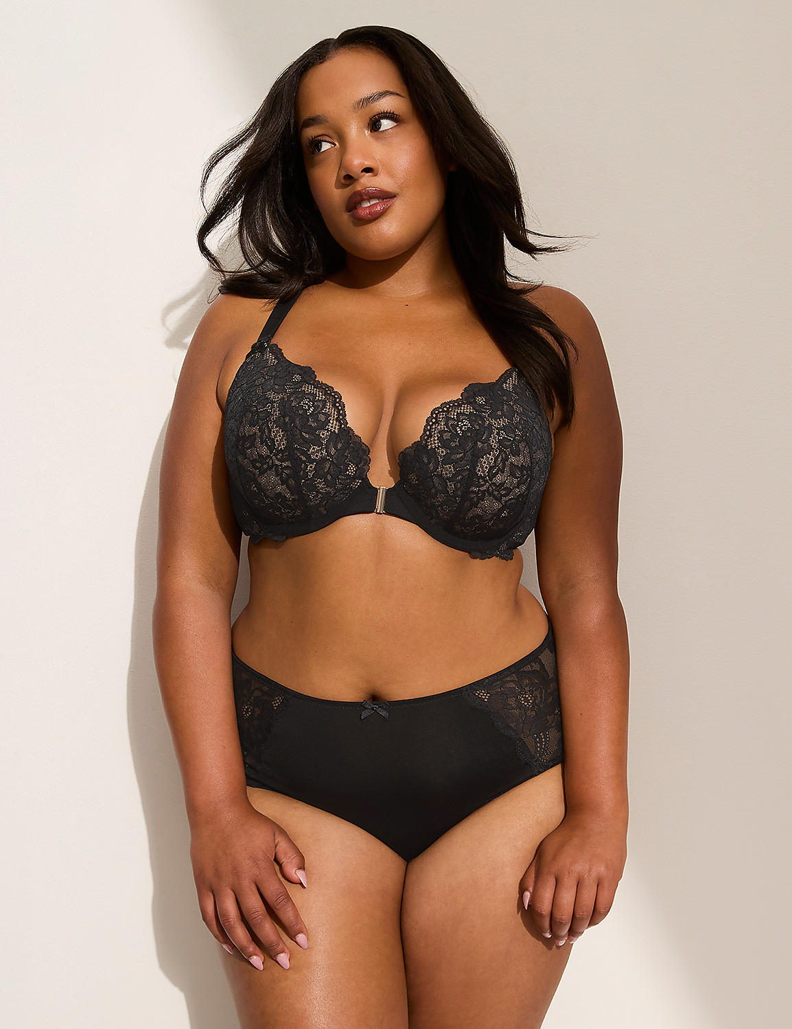 A woman in a black lace bra and matching underwear stands against a plain, light-colored wall with soft lighting. Product Image 4