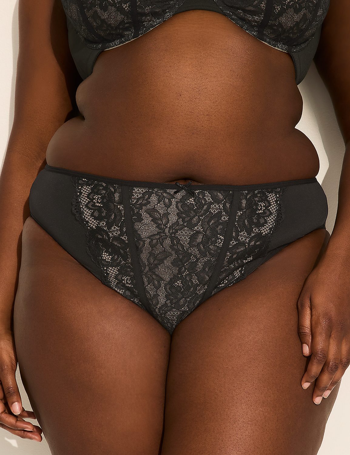A woman in black lace underwear stands against a plain, light-colored wall. Product Image 1