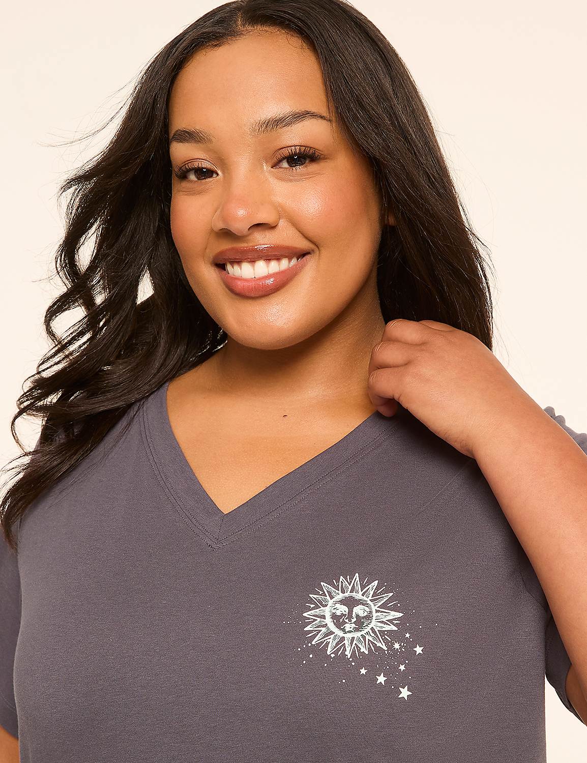 A smiling woman with dark hair is in the foreground, wearing a gray v-neck shirt with a sun and stars graphic, against a plain, light-colored background. Product Image 4