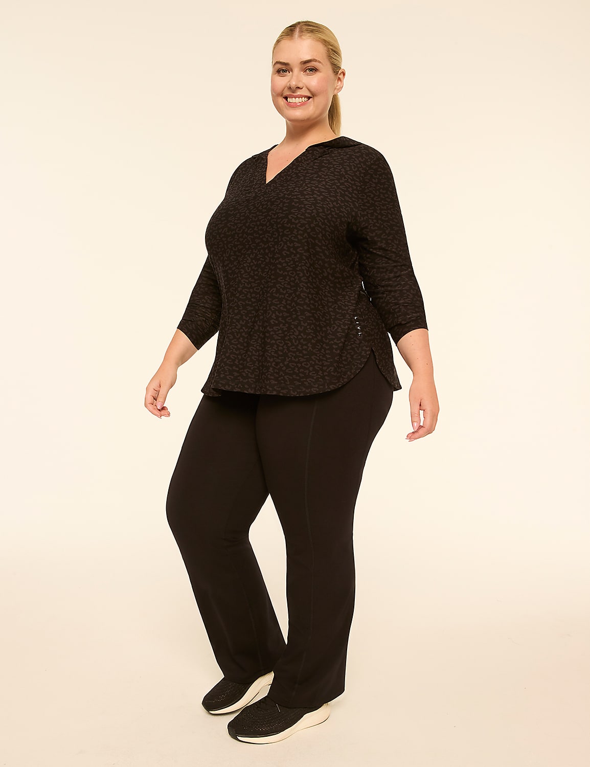A smiling woman in a patterned top and black pants stands against a plain, light-colored background. Product Image 3