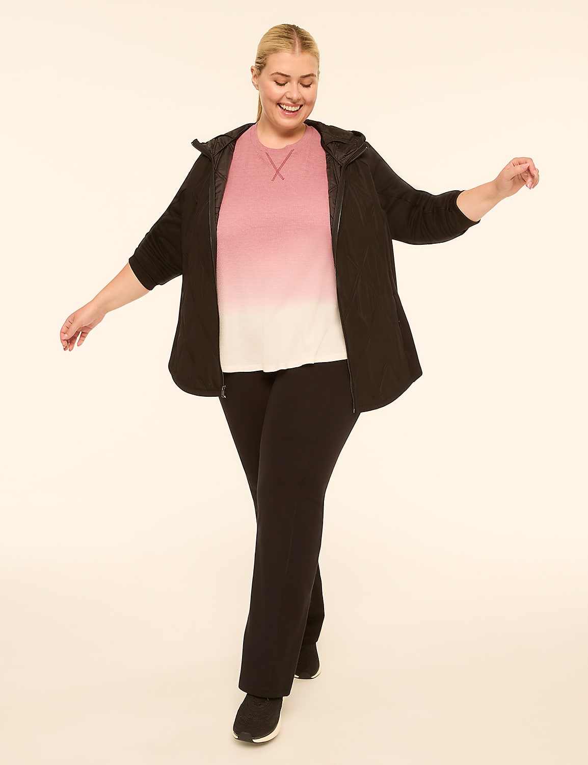 A smiling woman in a black zip-up jacket, pink and white ombre t-shirt, and black pants poses with her arms outstretched against a plain, light-colored background. Product Image 3