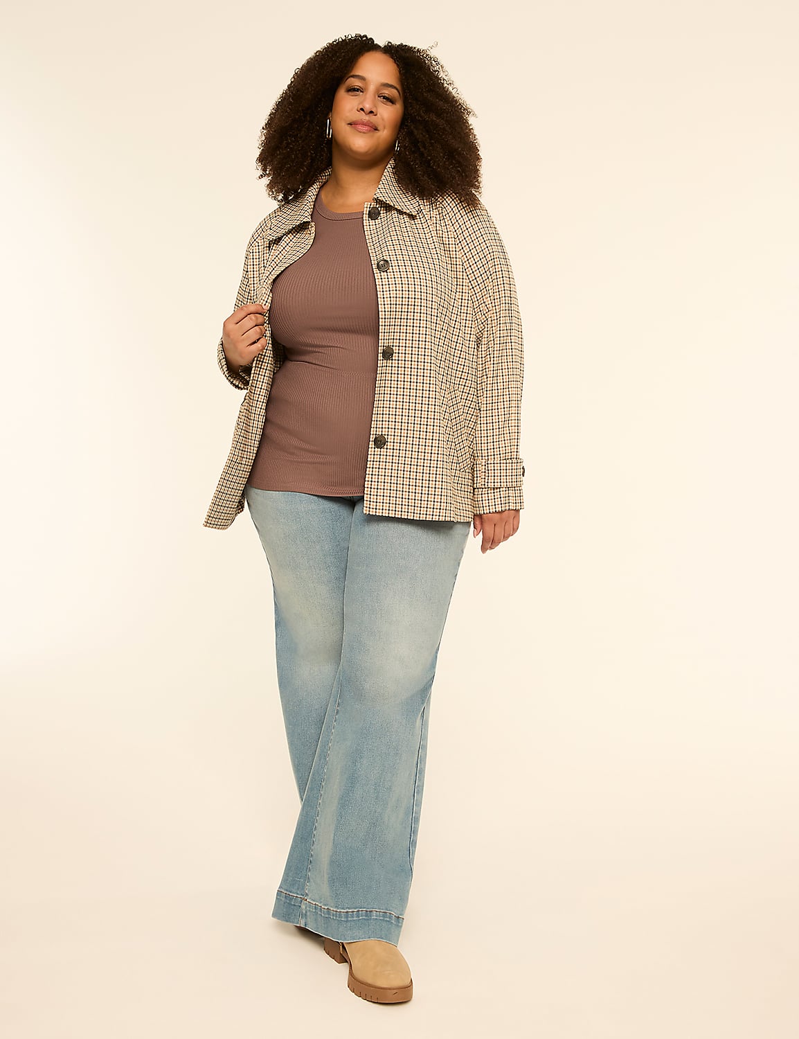 A woman with curly hair stands in the foreground wearing a plaid jacket and light-wash flared jeans against a plain, light-colored background. Product Image 3