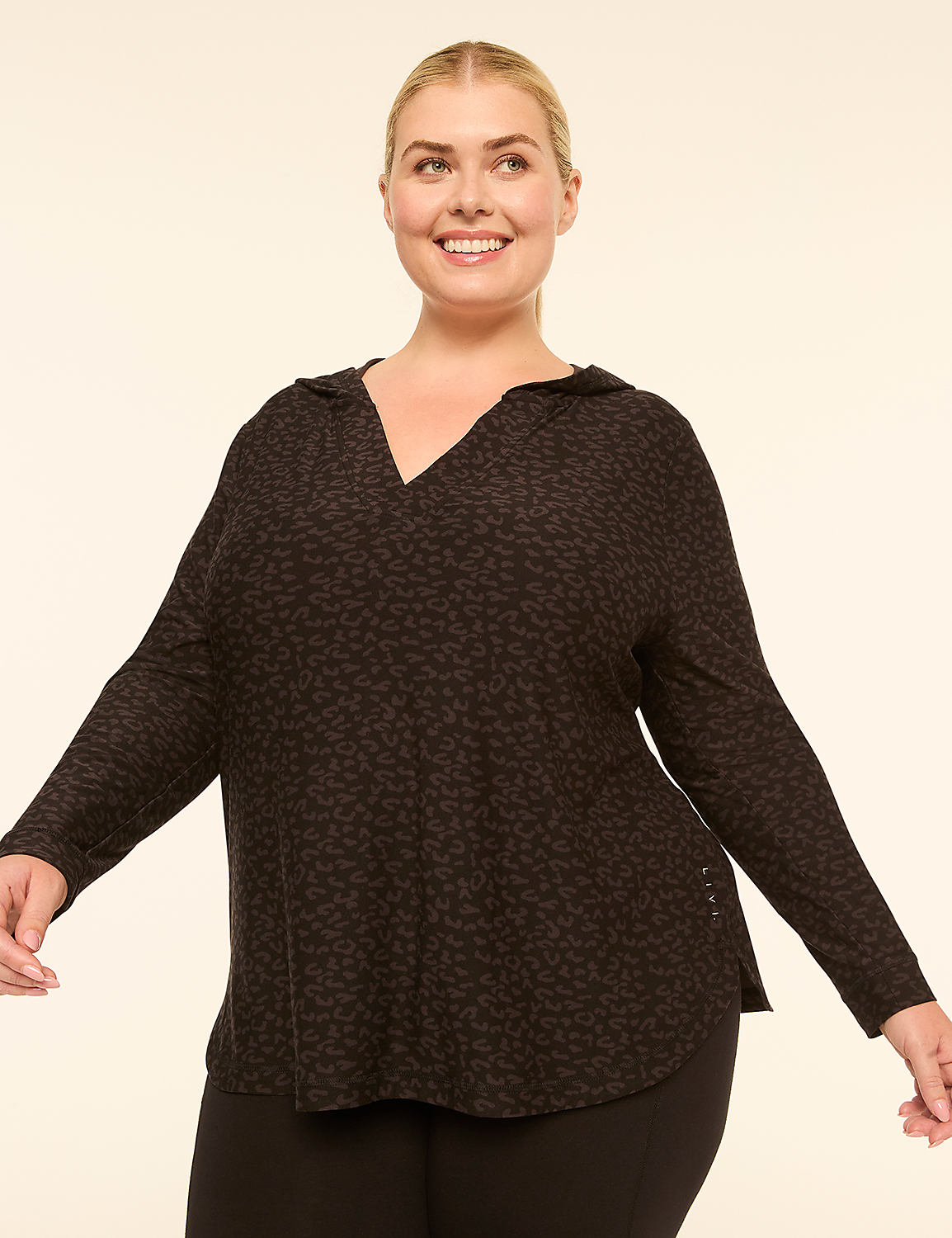 A smiling woman in a dark, leopard-print hooded top stands against a plain, light-colored background. Product Image 1