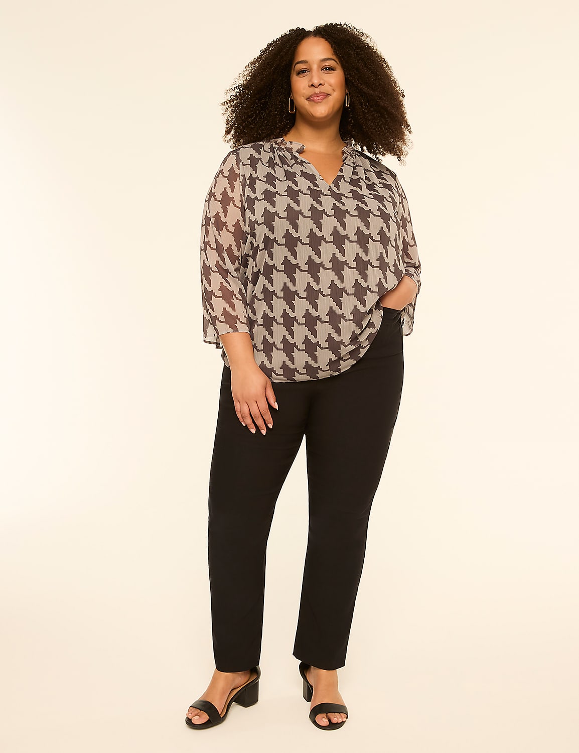 A woman with curly hair stands in the foreground wearing a houndstooth blouse and black pants against a plain, light-colored background. Product Image 3