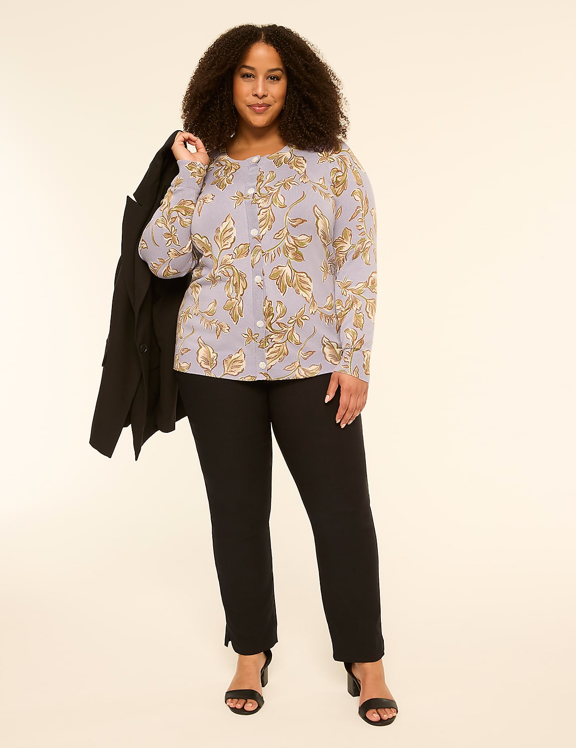 A woman in a floral cardigan and black pants stands against a plain, light-colored background, with a black jacket draped over her shoulder. Product Image 3