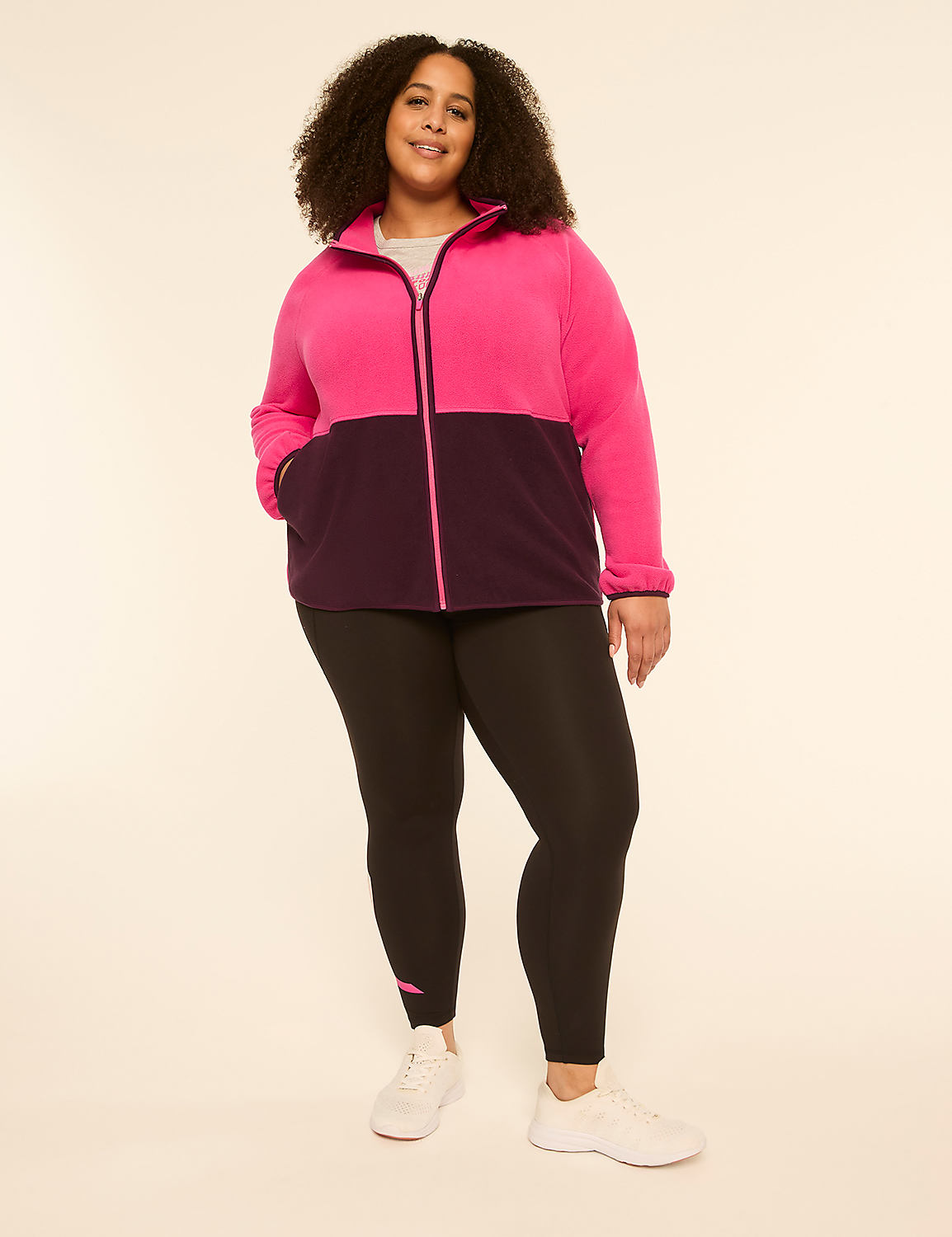 A woman in a pink and purple zip-up jacket and black leggings stands against a plain, light-colored background. Product Image 3
