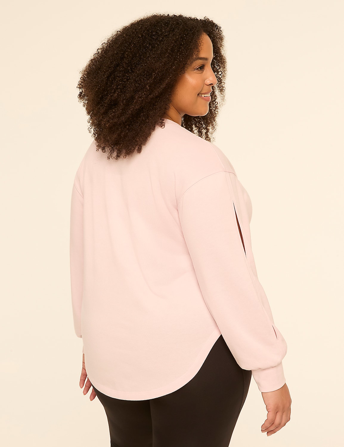 A woman with curly dark hair, wearing a light pink long-sleeved top and black leggings, stands against a plain, light-colored background. Product Image 2