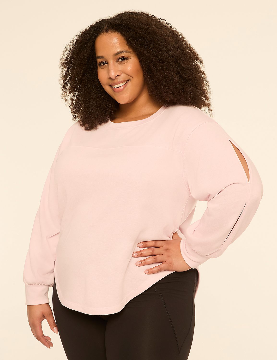 A smiling woman with curly hair poses in a light pink top and black leggings against a plain, light background. Product Image 1