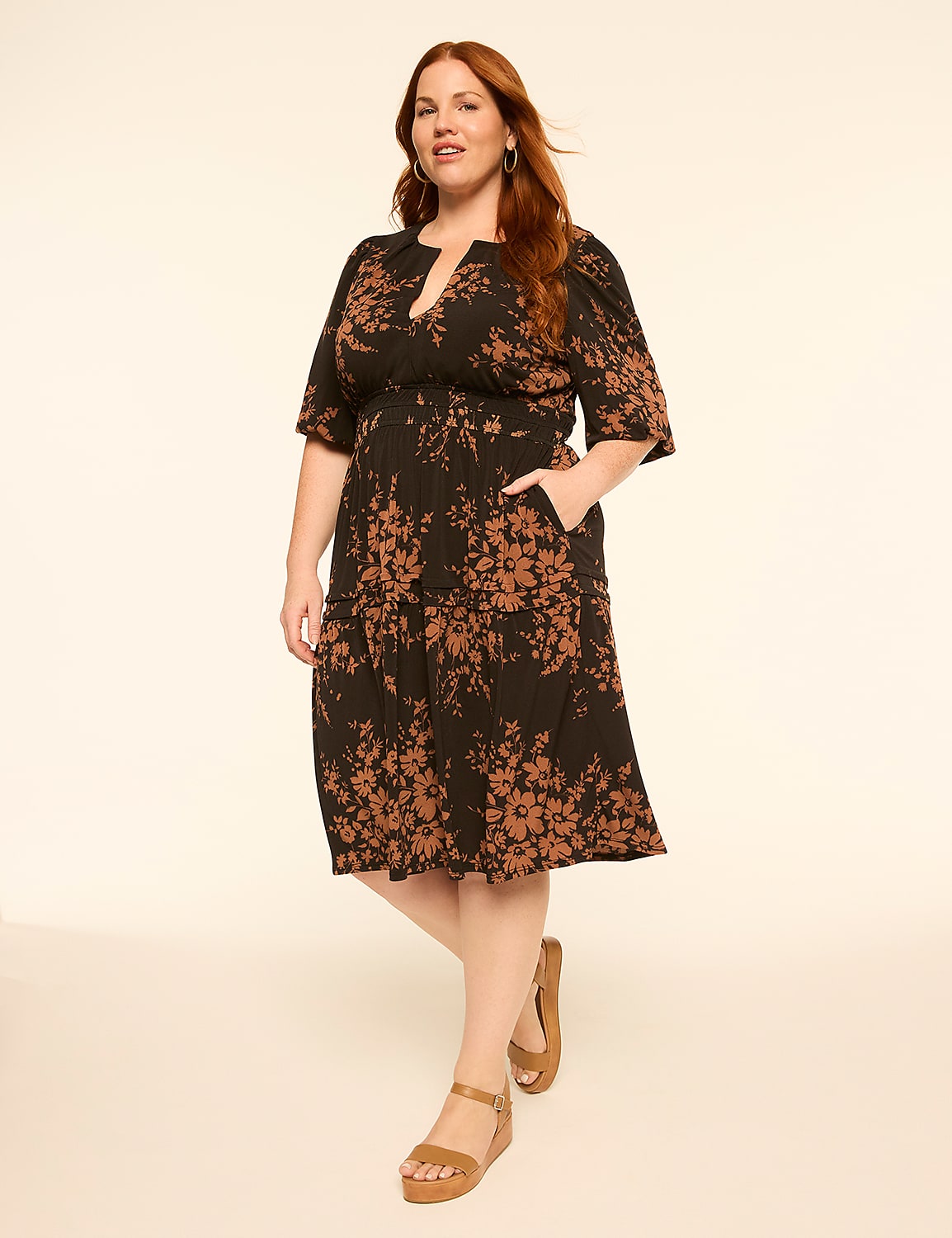 A woman in a floral print dress stands against a plain, light-colored background. Product Image 1