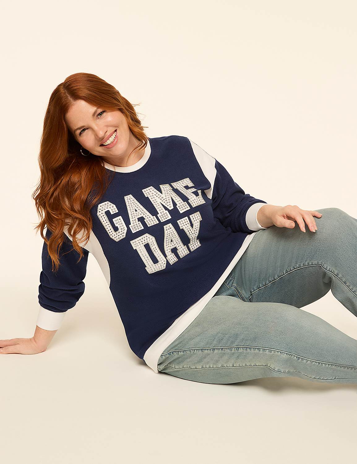 A smiling woman with red hair in a "GAME DAY" sweatshirt and jeans poses against a plain, light-colored background. Product Image 3