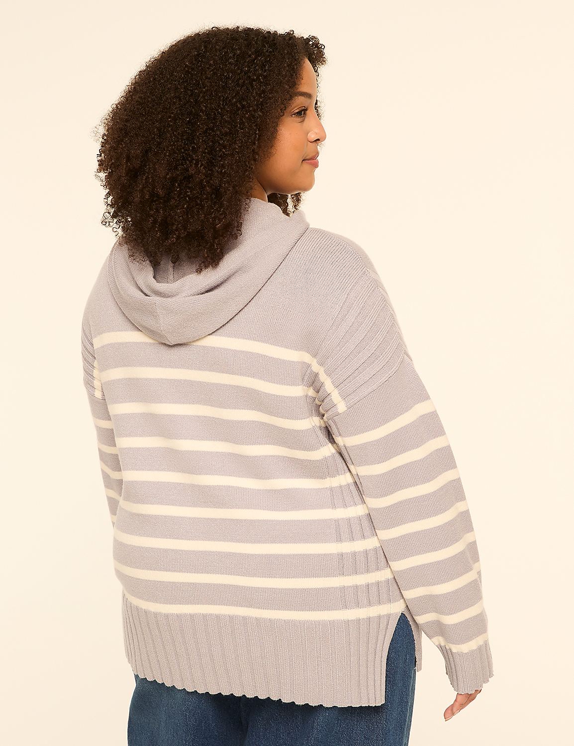 A young woman with curly hair, wearing a striped hooded sweater and blue jeans, stands against a plain, light-colored background. Product Image 2
