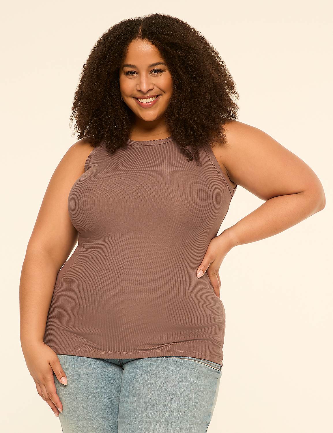 A smiling woman with curly hair in a brown tank top and jeans stands against a plain, light-colored background. Product Image 1