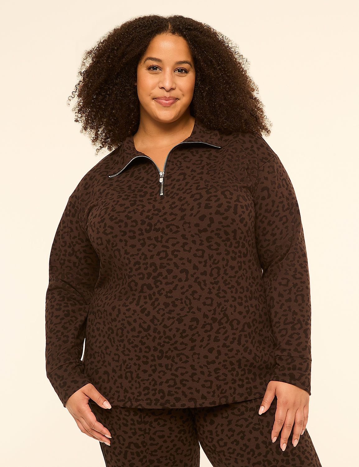 A woman with curly dark hair smiles at the camera, wearing a brown leopard-print quarter-zip sweatshirt and matching pants against a plain cream background. Product Image 1