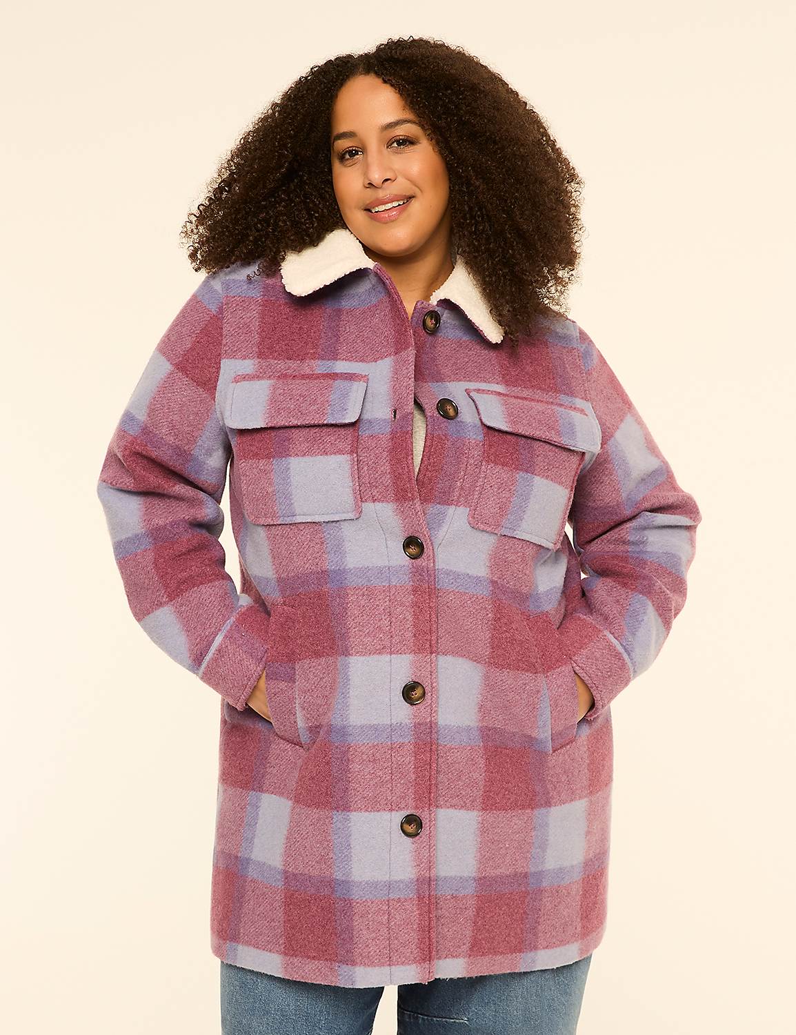 A smiling woman with curly hair stands in the foreground wearing a plaid jacket with a cream collar, against a plain cream background. Product Image 1