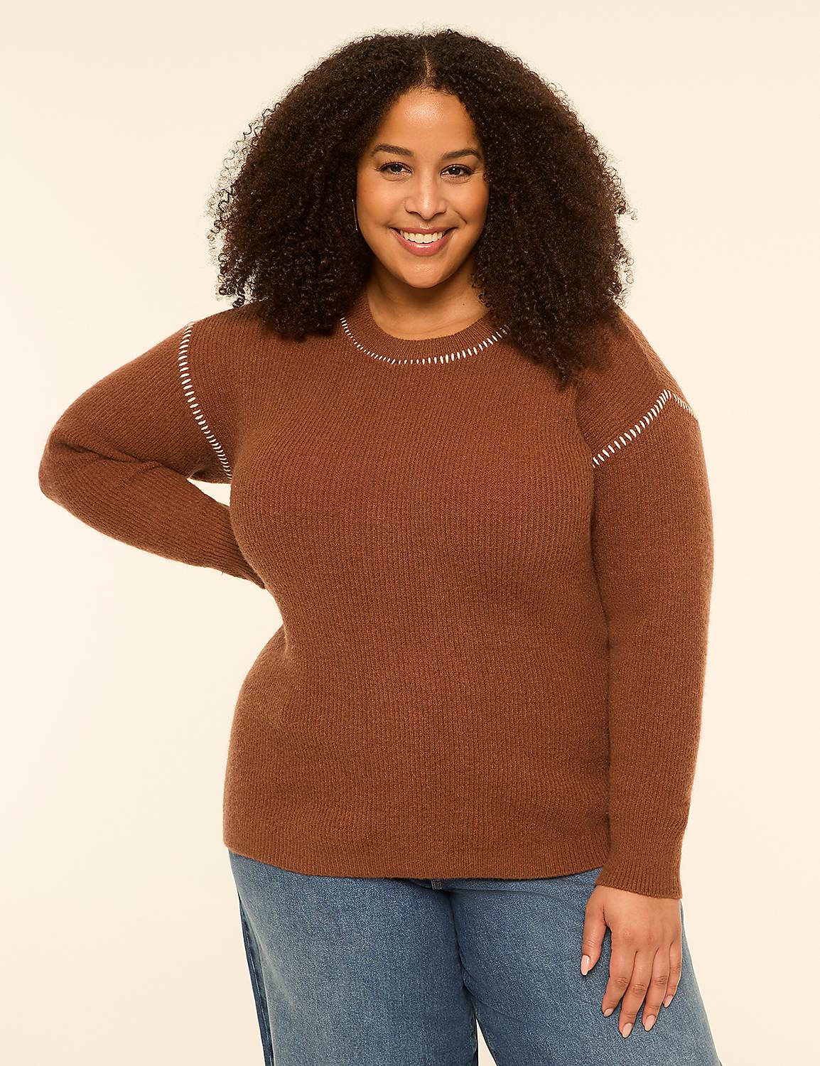 A smiling woman with curly hair wears a brown sweater and blue jeans against a plain, light-colored background. Product Image 1