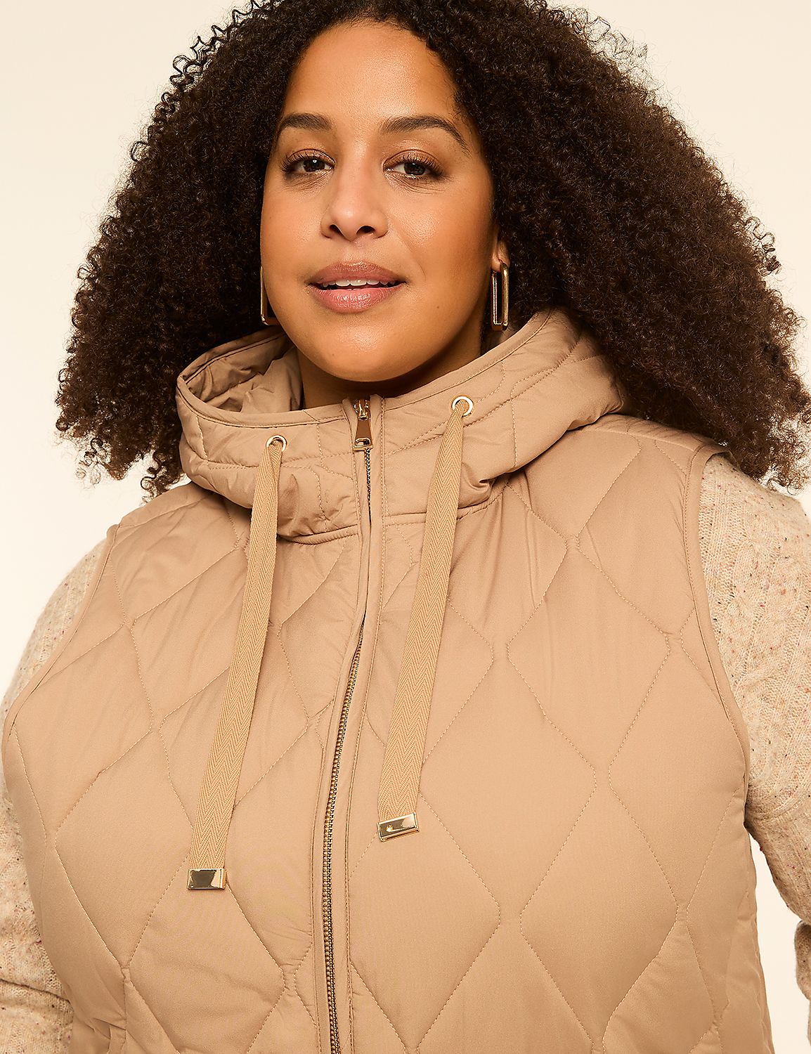 A woman with curly hair wears a tan quilted vest over a cream sweater, with a plain cream background. Product Image 3