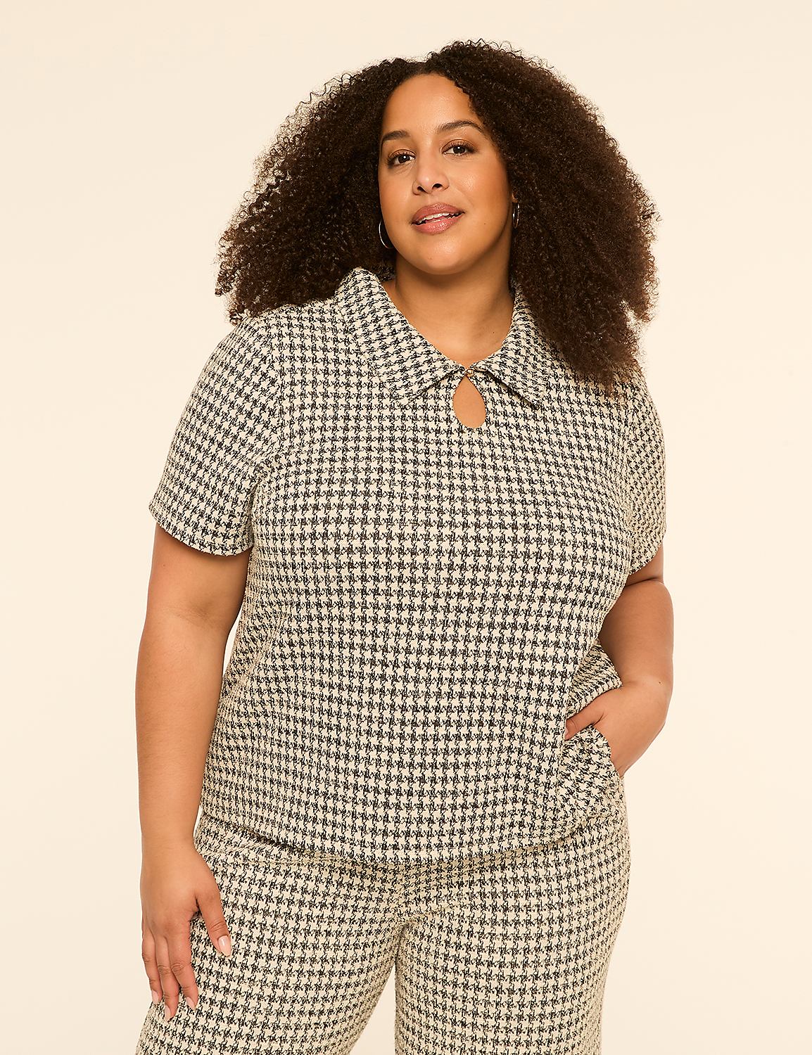 A woman with curly hair stands in the foreground wearing a houndstooth top and pants against a plain, light-colored background. Product Image 1