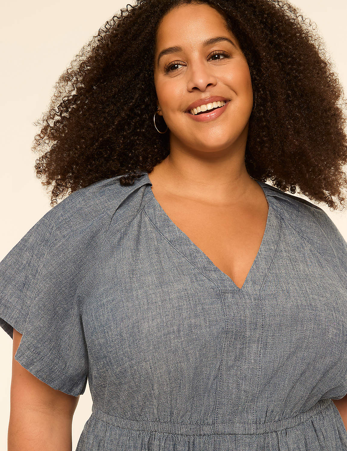 A smiling woman with curly hair wears a blue dress against a plain, light-colored background. Product Image 3