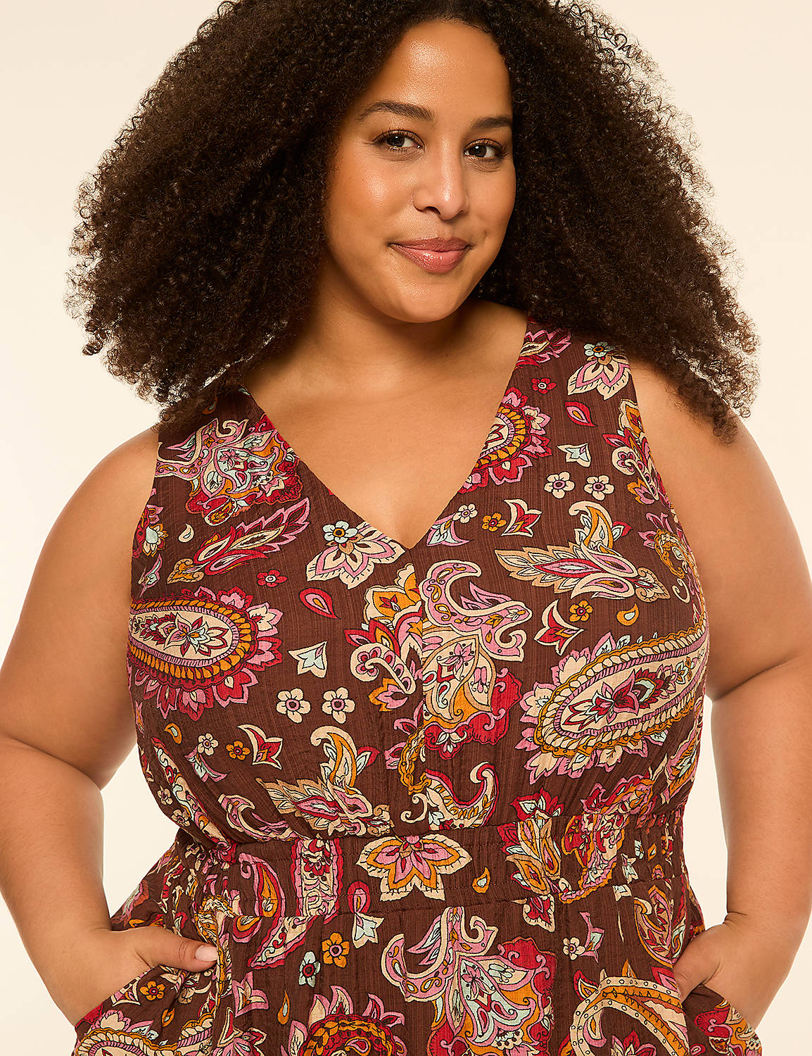 A woman with curly hair smiles at the camera, wearing a brown paisley-patterned dress with her hands in her pockets, against a plain, light-colored background. Product Image 3