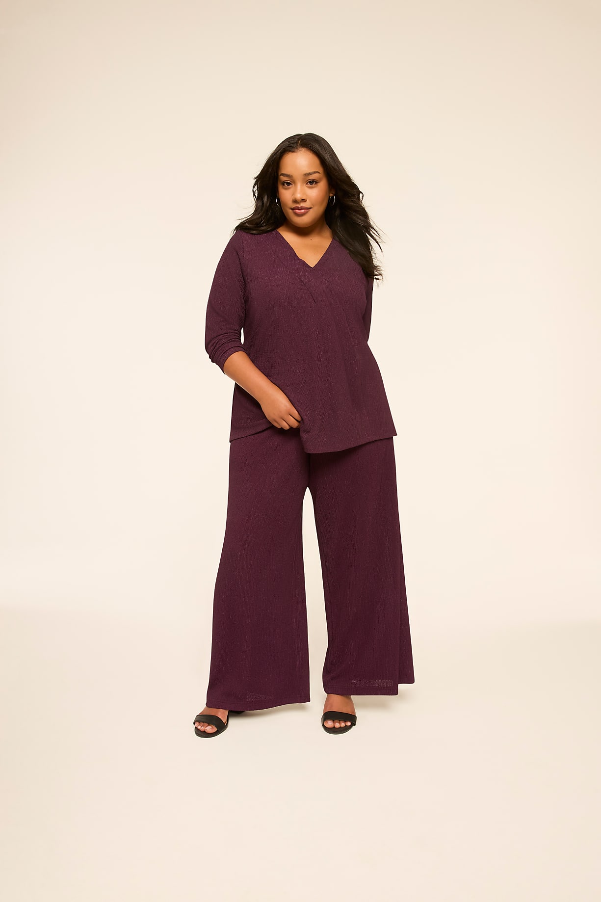 A woman in a plum-colored v-neck top and wide-leg pants stands against a plain, light-colored background. Product Image 4